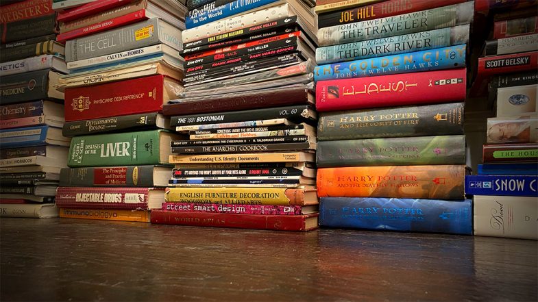 Stacks of books sit on a dark wooden floor