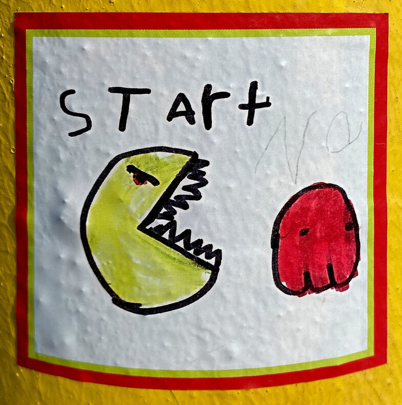 White sticker with red and yellow border with a pacman character chasing a red ghost. The word, "Start" is written above in a child's handwriting.