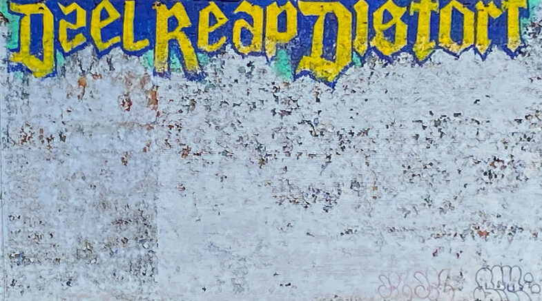 Large white painted brick wall with the words, "Deal Reap Distort" graffiti in gold and purple letters.