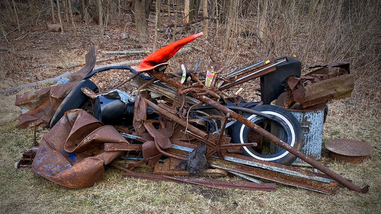 A pile of trash pulled from the local nature preserve. Items include tiles, a traffic cone, pipes, oil drums, trash cans, a manhole cover, plastic pots, fence posts and scrap metal.