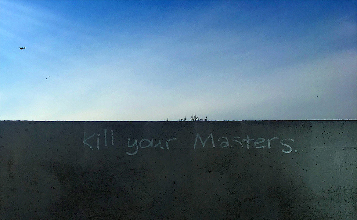 Graffiti lettering saying, "kill your masters" on a wall with blue sky behind
