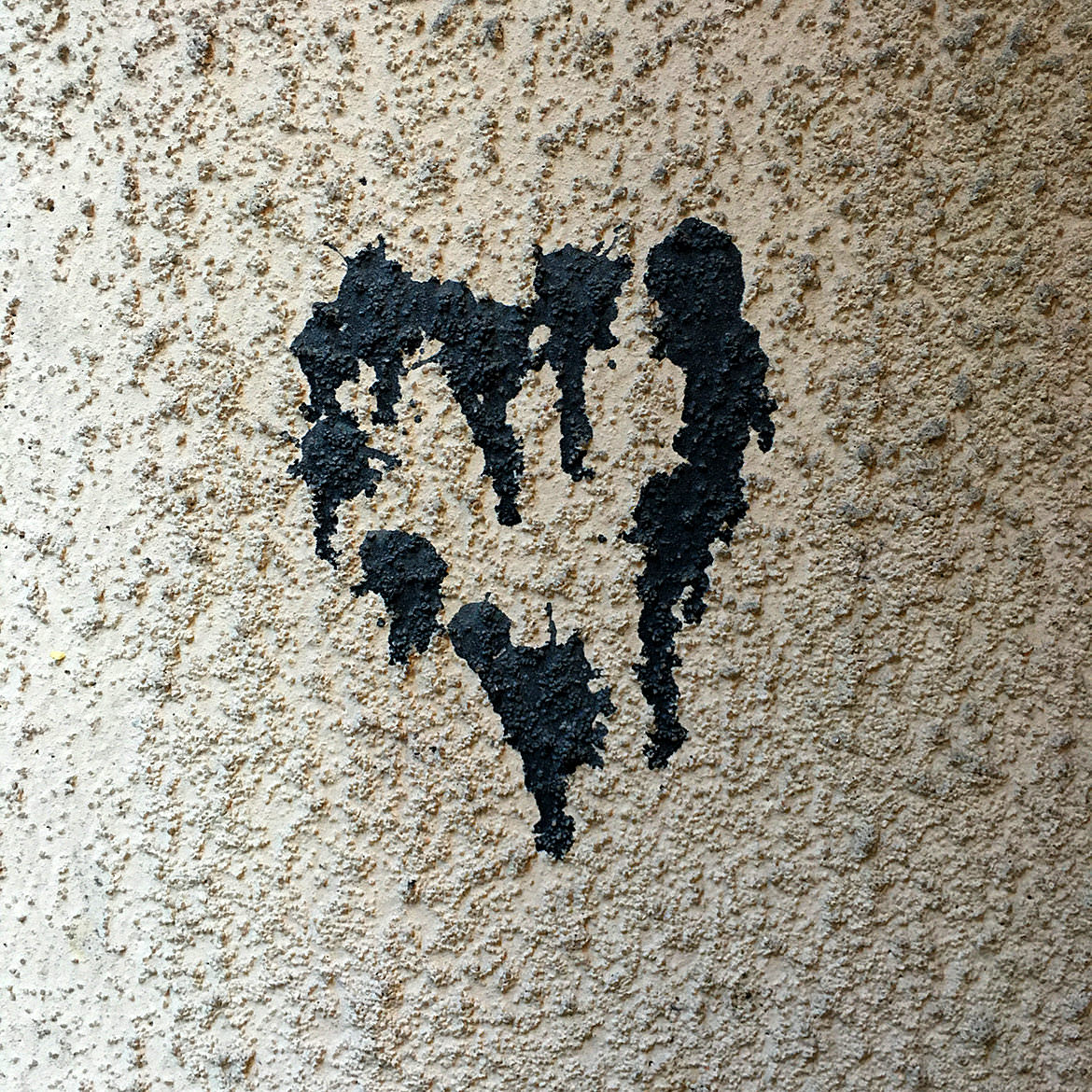 A black heart shape made of industrial glue remains on a stucco wall